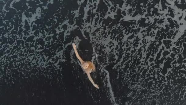 Vue aérienne d'une jeune femme marchant et s'amusant sur une plage avec un sable volcanique noir 