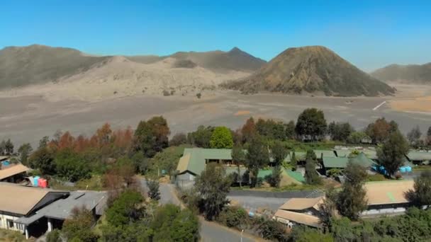 Aerial view on famous active Bromo volcano or Mount Gunung Bromo and Batok volcano inside the Tengger caldera on the Java island. Drone flies at the edge of the caldera where the village is situated — Stock Video