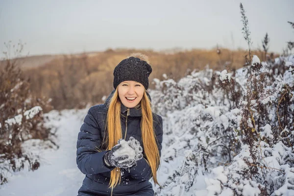 winter girl throwing snowball at camera smiling happy having fun outdoors on snowing winter day playing in snow. Cute playful young woman outdoor enjoying first snow