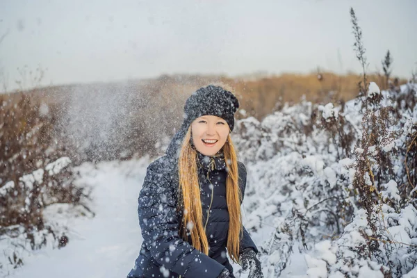 winter girl throwing snowball at camera smiling happy having fun outdoors on snowing winter day playing in snow. Cute playful young woman outdoor enjoying first snow