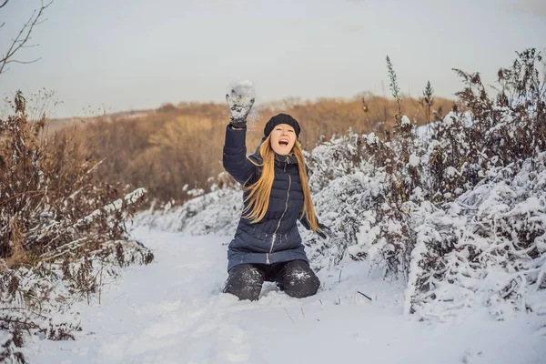 Winter girl throwing snowball at camera smiling happy having fun outdoors on snowing winter day playing in snow. Cute playful young woman outdoor enjoying first snow — Stock Photo, Image