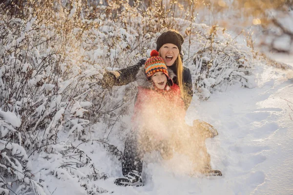 Tél Anya és fia dobott hógolyó a kamera mosolyogva boldog szórakozás szabadban havazás téli nap játszik a hóban. Aranyos játékos fiatal nő szabadban élvezi az első hó — Stock Fotó