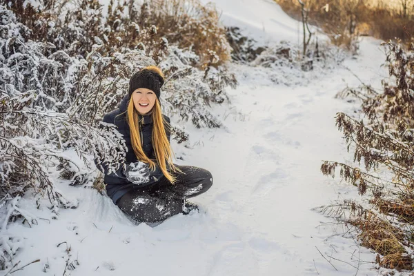 Chica de invierno lanzando bola de nieve a la cámara sonriendo feliz divirtiéndose al aire libre en el día de invierno nevando jugando en la nieve. Linda joven juguetona al aire libre disfrutando de la primera nieve — Foto de Stock