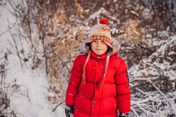 Pojke i röda kläder som leker utomhus. Aktiv fritid med barn på vintern under kalla dagar. Pojken har kul med första snön. Glad liten unge leker i snö, bra vinterväder — Stockfoto
