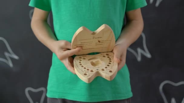 Маленький хлопчик показує дерев'яну коробку для молочних зубів. Концепція зміни дитячого зуба — стокове відео