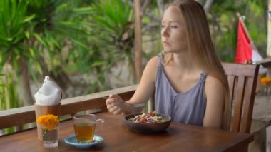 Tropik bir kafede genç bir kadın sağlıklı vejetaryen salatası yiyor. Vejetaryen gıda konsepti