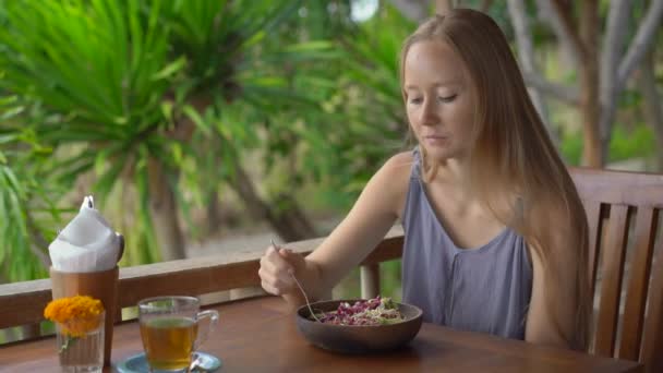 Una joven en un café tropical come ensalada vegetariana saludable. Concepto de comida vegana — Vídeos de Stock