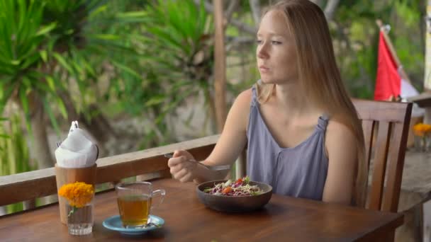 Una joven en un café tropical come ensalada vegetariana saludable. Concepto de comida vegana — Vídeos de Stock