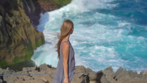 Jonge vrouw toerist bezoekt het Angels Billabong strand op het Nusa Penida eiland waar enorme golven breken op de rotsen. Langzame schot — Stockvideo