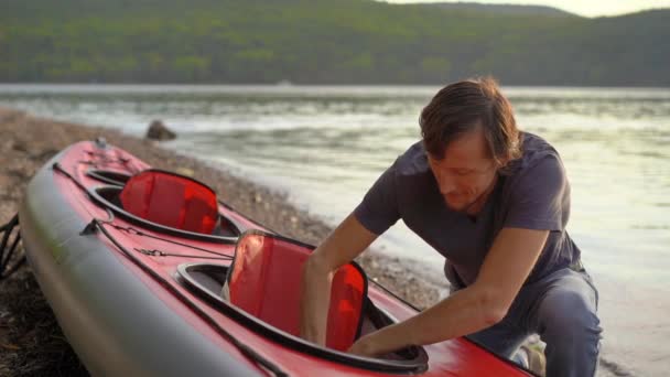 Unge man blåser upp sin kajak och förbereder den för paddling i sjö eller hav. Slowmotion skott — Stockvideo