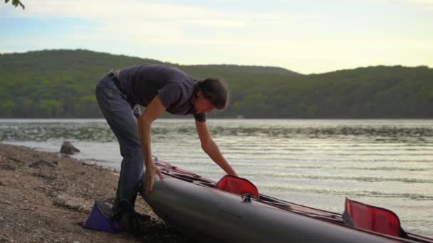El joven infla su kayak y lo prepara para remar en un lago o mar. Disparo en cámara lenta — Vídeo de stock
