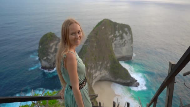 若い女性の観光客は、インドネシアのヌサペニダ州ケリングキングビーチのいわゆるティラノサウルス岩を訪れます。ヌサペニダ島の有名な観光地。スローモーションショット — ストック動画