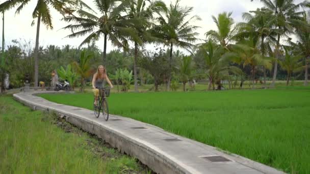 一个年轻的女人骑自行车穿过美丽的稻田. 前往东南亚的旅行概念。 慢动作射击 — 图库视频影像