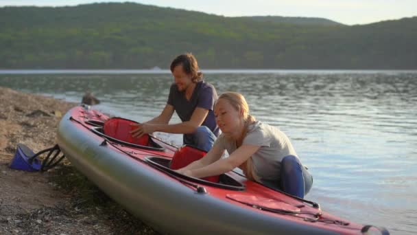 Młody mężczyzna i kobieta przygotowują swój nadmuchiwany kajak do pływania w jeziorze lub morzu. Strzał zwolniony — Wideo stockowe