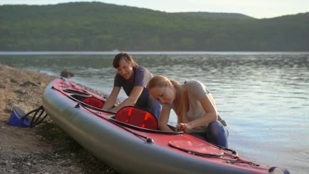 Jongeman en vrouw bereiden hun opblaasbare kajak voor om te peddelen in een meer of zee. Langzame schot — Stockvideo