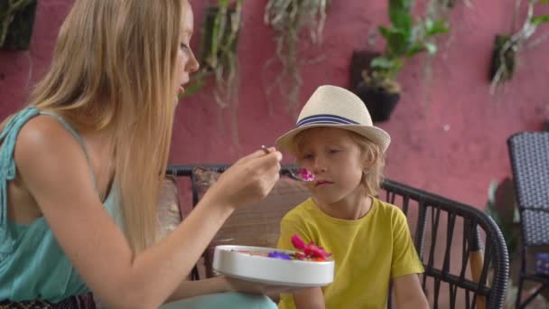 Genç bir kadın ve küçük oğlu güzel bir kafede oturmuş renkli granola kokteylinin tadını çıkarıyorlar. Sağlıklı beslenme konsepti. Yavaş çekim. — Stok video