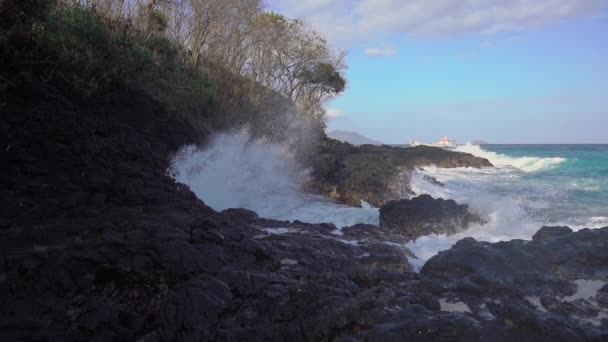Ein schwarzer Vulkanstrand. Wellen krachen auf die Felsen und lassen einen natürlichen Springbrunnen entstehen. Zeitlupenschuss — Stockvideo