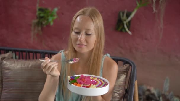 年轻的女人坐在漂亮的咖啡店里，坐在碗里，享受着五彩缤纷的格拉诺拉冰沙。 健康饮食的概念。 慢动作射击 — 图库视频影像