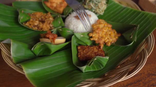 El joven y su pequeño hijo comen comida balenesa tradicional en un café tradicional. Viajes al concepto de Bali — Vídeo de stock