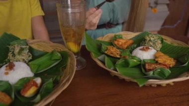Genç bir kadın ve küçük oğlu geleneksel bir kafe olan Nasi Campur 'da geleneksel Bali yemekleri yiyorlar. Bali konseptine Seyahat