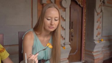 Genç bir kadın ve küçük oğlu geleneksel bir kafe olan Nasi Campur 'da geleneksel Bali yemekleri yiyorlar. Bali konseptine Seyahat