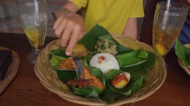 Genç adam ve küçük oğlu geleneksel Bali yemekleri yiyorlar Nasi Campur 'da geleneksel bir kafede. Bali konseptine Seyahat