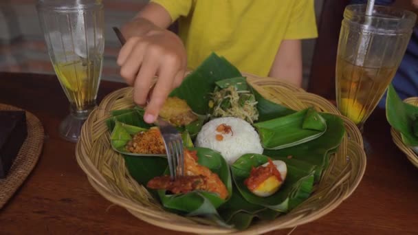 Jongeman en zijn zoontje eten traditionele Balenese gerechten en zetten Nasi Campur in een traditioneel café. Reis naar Bali concept — Stockvideo