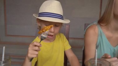 Genç bir kadın ve küçük oğlu geleneksel bir kafe olan Nasi Campur 'da geleneksel Bali yemekleri yiyorlar. Bali konseptine Seyahat
