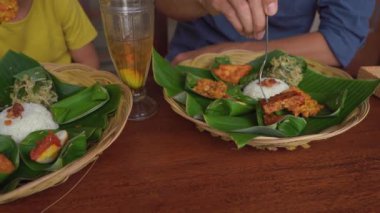 Genç adam ve küçük oğlu geleneksel Bali yemekleri yiyorlar Nasi Campur 'da geleneksel bir kafede. Bali konseptine Seyahat