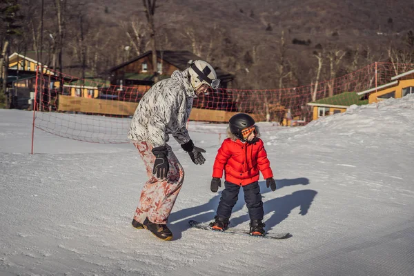 Apa snowboardozni tanítja a fiát. Tevékenységek gyerekeknek télen. Gyermek téli sport. Életmód — Stock Fotó