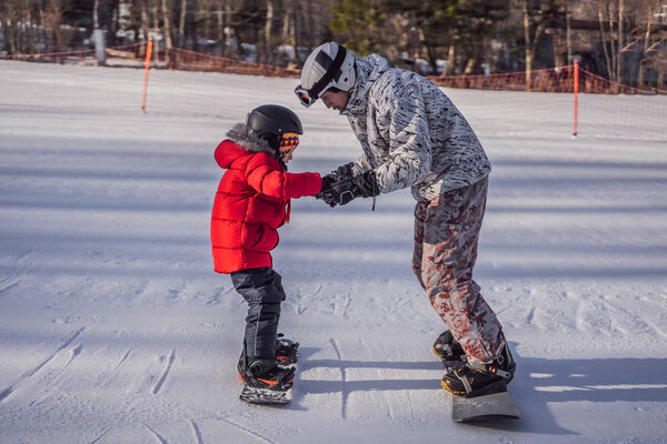Dad teaches son snowboarding. Activities for children in winter. Childrens winter sport. Lifestyle
