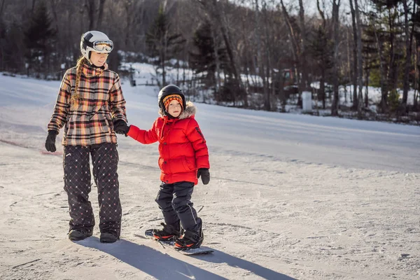 A mãe ensina snowboard ao filho. Atividades para crianças no inverno. Desporto de inverno das crianças. Estilo de vida — Fotografia de Stock