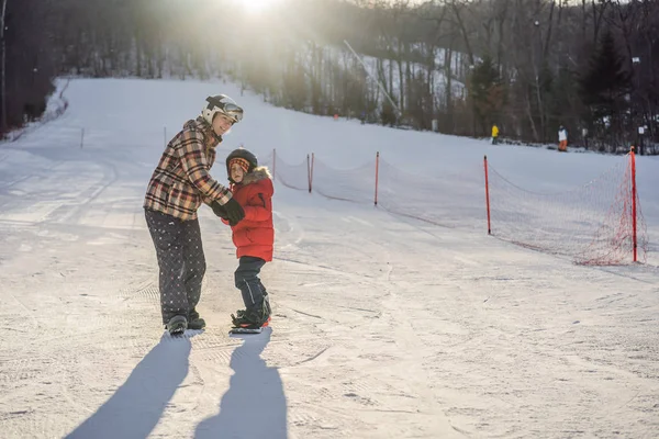 Matka uczy syna snowboardingu. Zajęcia dla dzieci w zimie. Zimowy sport dla dzieci. Styl życia — Zdjęcie stockowe