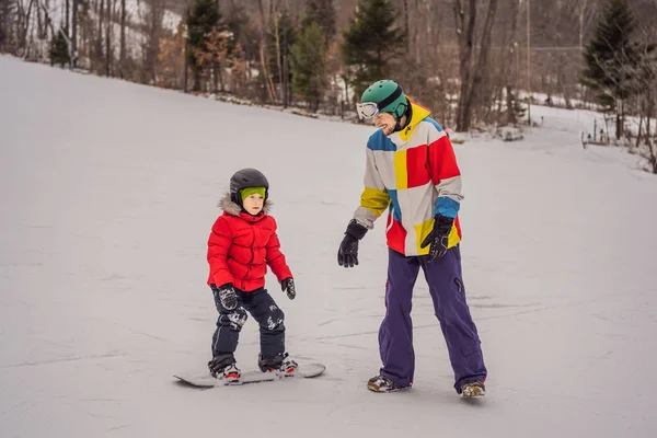 Ο δάσκαλος του snowboard μαθαίνει σε ένα αγόρι να κάνει snowboard. Δραστηριότητες για παιδιά το χειμώνα. Παιδικό χειμερινό άθλημα. Τρόπος ζωής — Φωτογραφία Αρχείου