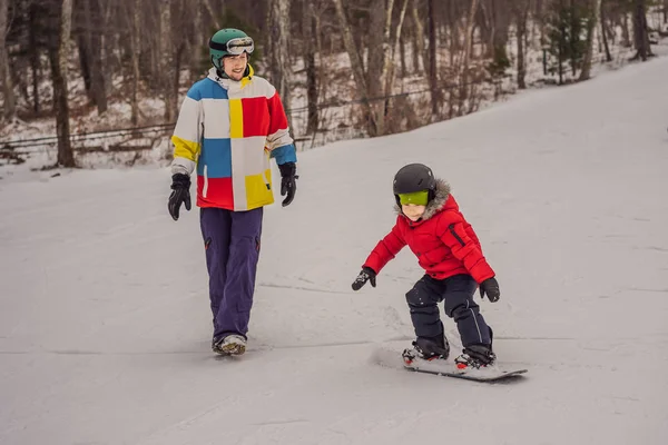 Ο δάσκαλος του snowboard μαθαίνει σε ένα αγόρι να κάνει snowboard. Δραστηριότητες για παιδιά το χειμώνα. Παιδικό χειμερινό άθλημα. Τρόπος ζωής — Φωτογραφία Αρχείου