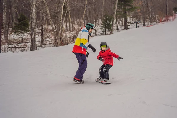 Un moniteur de snowboard enseigne le snowboard à un garçon. Activités pour les enfants en hiver. Sport d'hiver pour enfants. Mode de vie — Photo