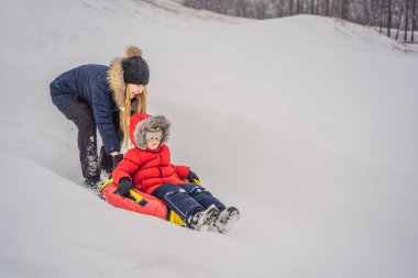 Anne oğul şişme bir kış kızağı borusuna biniyor. Tüm aile için kış eğlencesi