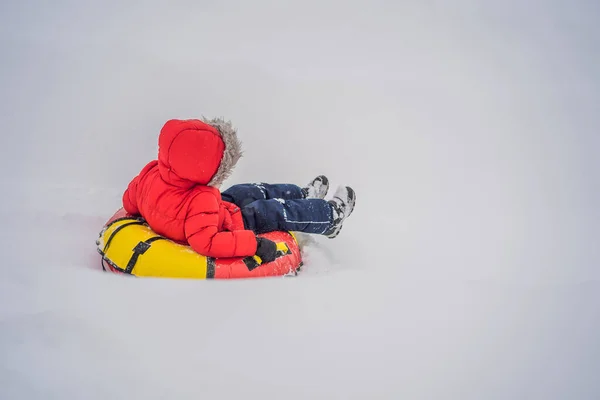 Niño divirtiéndose en tubo de nieve. El chico está montando un tubo. Diversión de invierno para niños —  Fotos de Stock