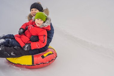 Anne oğul şişme bir kış kızağı borusuna biniyor. Tüm aile için kış eğlencesi