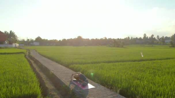 Luchtfoto van een jonge vrouw die yoga beoefent op een groot mooi rijstveld bij zonsondergang. Reizen naar Azië concept. — Stockvideo