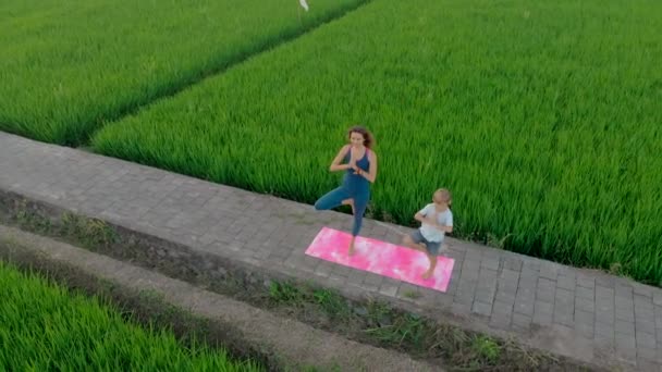 Luchtfoto van een jonge vrouw yoga trainer onderwijzen kleine jongen op een groot mooi rijstveld tijdens zonsondergang. Reizen naar Azië concept. — Stockvideo