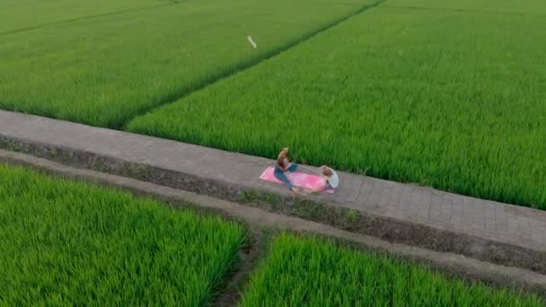 Luchtfoto van een jonge vrouw yoga trainer onderwijzen kleine jongen op een groot mooi rijstveld tijdens zonsondergang. Reizen naar Azië concept. — Stockvideo