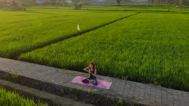 Luchtfoto van een jonge vrouw die yoga beoefent op een groot mooi rijstveld bij zonsondergang. Reizen naar Azië concept. — Stockvideo