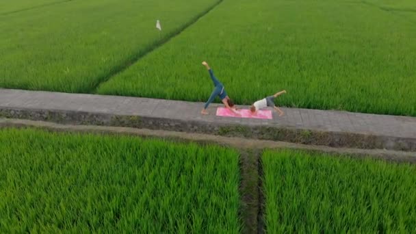 Luchtfoto van een jonge vrouw yoga trainer onderwijzen kleine jongen op een groot mooi rijstveld tijdens zonsondergang. Reizen naar Azië concept. — Stockvideo