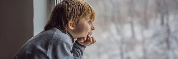 Felice adorabile bambino seduto vicino alla finestra e guardando fuori sulla neve il giorno di Natale o la mattina. Bambino sorridente affascinato dalle nevicate e dai grandi fiocchi di neve BANNER, FORMATO LUNGO — Foto Stock