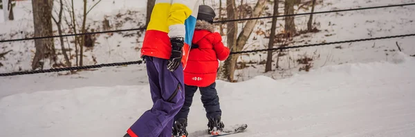 Istruttore di snowboard insegna a un ragazzo a fare snowboard. Attività per bambini in inverno. Sport invernali per bambini. Stile di vita BANNER, FORMATO LUNGO — Foto Stock