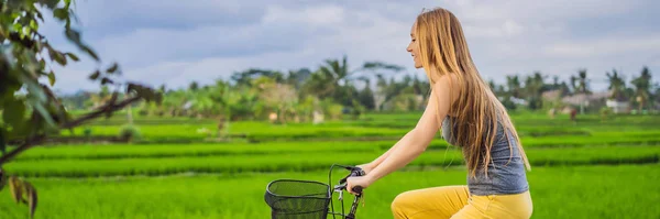 Eine junge frau fährt mit dem fahrrad auf einem reisfeld in ubud, bali. Bali Reisekonzept Banner, Langformat — Stockfoto