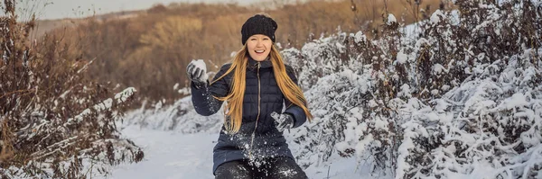 Chica de invierno lanzando bola de nieve a la cámara sonriendo feliz divirtiéndose al aire libre en el día de invierno nevando jugando en la nieve. Linda joven juguetona al aire libre disfrutando de la primera nieve BANNER, FORMATO LARGO —  Fotos de Stock