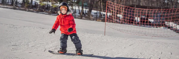 Aranyos fiú snowboardozik. Tevékenységek gyerekeknek télen. Gyermek téli sport. Életmód zászló, hosszú formátum — Stock Fotó