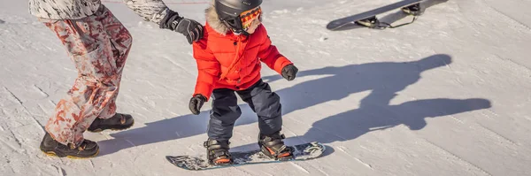 Papá enseña snowboard a su hijo. Actividades para niños en invierno. Deporte de invierno para niños. Estilo de vida BANNER, FORMATO LARGO — Foto de Stock